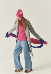 Siv plašč iz volne z ročnim vezenjem cvetlic, roza pletena kapa, roza pulover, široki modri kavbojki in pisana ruta. Tenisice z obročki.