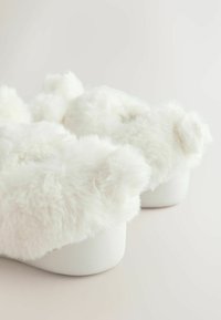 Weiße, pelzgefütterte Hausschuhe mit einer weichen, flauschigen Textur und runden Akzenten. Die Sohle ist schneeweiß und ergänzt das flauschige Oberdesign.