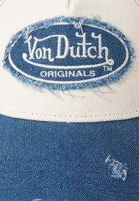 Denimist ja puuvillast müts, millel on valge eesmine paneel, kus on sinine kulunud plekk, millel on kirjas "Von Dutch ORIGINALS", ja kulunud tume sinine ääres.