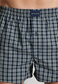 Marineblaue karierte Baumwollboxershorts mit elastischem Bund, einem Knopfverschluss und einem kontrastierenden weißen und grünen Karomuster.