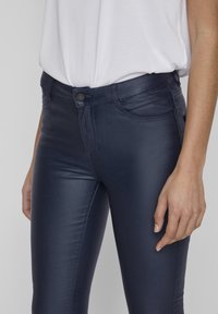 Pantalones ajustados de color azul marino, hechos de un material suave y elástico. Incluyen bolsillos frontales, cierre por botón y detalles de costura sutiles.