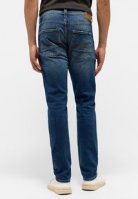 Blå denimjeans med rak bendesign, som har två bakfickor med gul sömnad och en läderetikett vid midjan.
