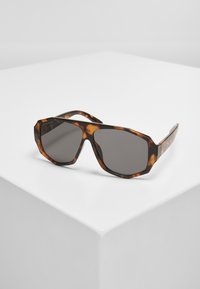 Lunettes de soleil en écaille de tortue avec une monture octogonale, verres gris et finition lisse. Les accents comprennent des motifs texturés subtils sur les branches.