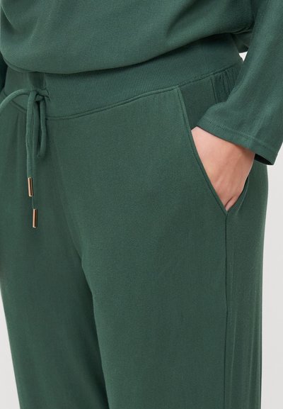 Green sweatpants with a drawstring waist, ribbed texture, two side pockets, and gold-tone hardware accents. Close-up view of the fabric.