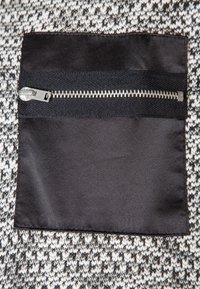 Svart dragkedjeficka på ett texturerat tyg med ett monokromt hundtandsmönster. Dragkedjan har metalltänder och en dragflik.