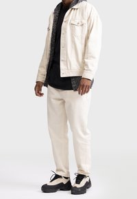 Veste en denim crème avec doublure texturée noire, associée à un t-shirt noir et un pantalon crème. Baskets noires avec une semelle épaisse.