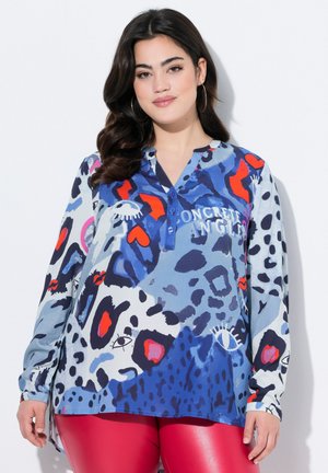 Blusa a maniche lunghe in un tessuto blu chiaro con audaci motivi astratti in rosso, nero e blu navy, caratterizzata da una placca di bottoni e un orlo arrotondato.