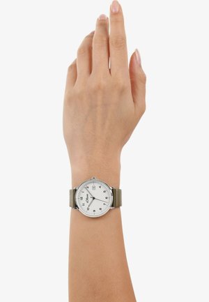 Zilveren horloge met een witte wijzerplaat, grijze cijfers en een datumaanduiding. Het heeft een zachte, gestructureerde grijze stoffen strap.