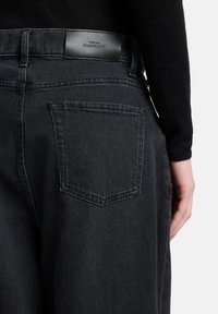 Ciemne dżinsy z prostą nogawką. Charakteryzują się czarną skórzaną etykietą na pasku biodrowym oraz pojedynczą tylną kieszenią.