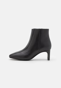 Bota de piel negra hasta el tobillo con puntera puntiaguda, tacón alto delgado y un diseño sin costuras. Presenta una costura mínima y una textura suave.