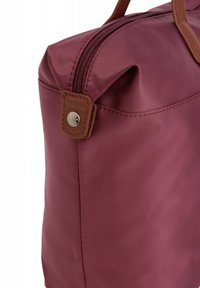 Borsa di tessuto bordeaux con accenti in pelle marrone, chiusura con zip e finitura lucida. Cuciture robuste lungo i bordi e dettaglio in metallo con clip.