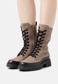 Lace-up enkellaarzen in taupe suede met zwarte accenten. Voorzien van een dikke zwarte zool en een ritssluiting aan de zijkant voor gemakkelijk aan- en uittrekken.