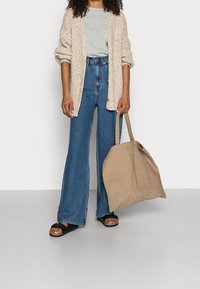 Beige stickad cardigan, ljusgrå t-shirt, högmidjade blå utsvängda jeans, svarta slidesandaler och en stor beige kanvasväska.