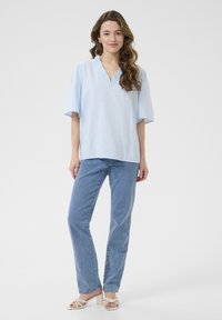Haut bleu clair à manches courtes avec un col en V et un col volé, associé à un jean bleu et des sandales à talons carrés blanches.