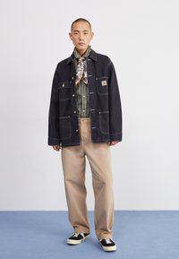 Dark denim jacket with four pockets, green and white striped shirt, beige wide-leg pants, and black sneakers with white sole.