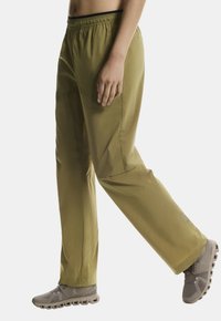 Olivengrüne, locker sitzende Hose mit elastischem Bund und seitlichen Taschen, aus leichtem Stoff; kombiniert mit braunen Sportschuhen.