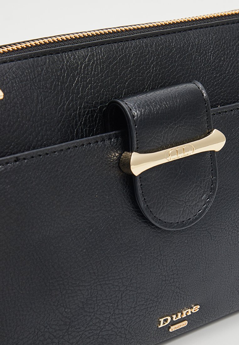 Zwarte leren tas met een textuur, voorzien van een sluiting met goudkleurig beslag en een gegraveerd logo. Heeft een klep met een drukknoop voor een veilige sluiting.