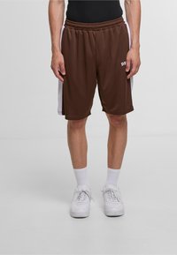 Shorts de sport marron avec des panneaux latéraux blancs, en tissu en maille, avec une taille élastique et un logo. Associés à des baskets blanches et des chaussettes.