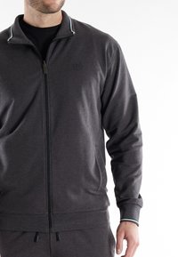 Chaqueta de cremallera gris oscuro con una textura suave, cuello alto y detalles de rayas blancas y azules en el cuello y los puños.