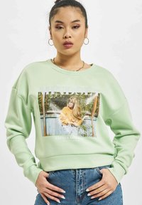 Lys grønn sweatshirt med frontgrafikk, rund hals og avslappet passform. Merkeverdig tekst og bilder komplementerer designet.
