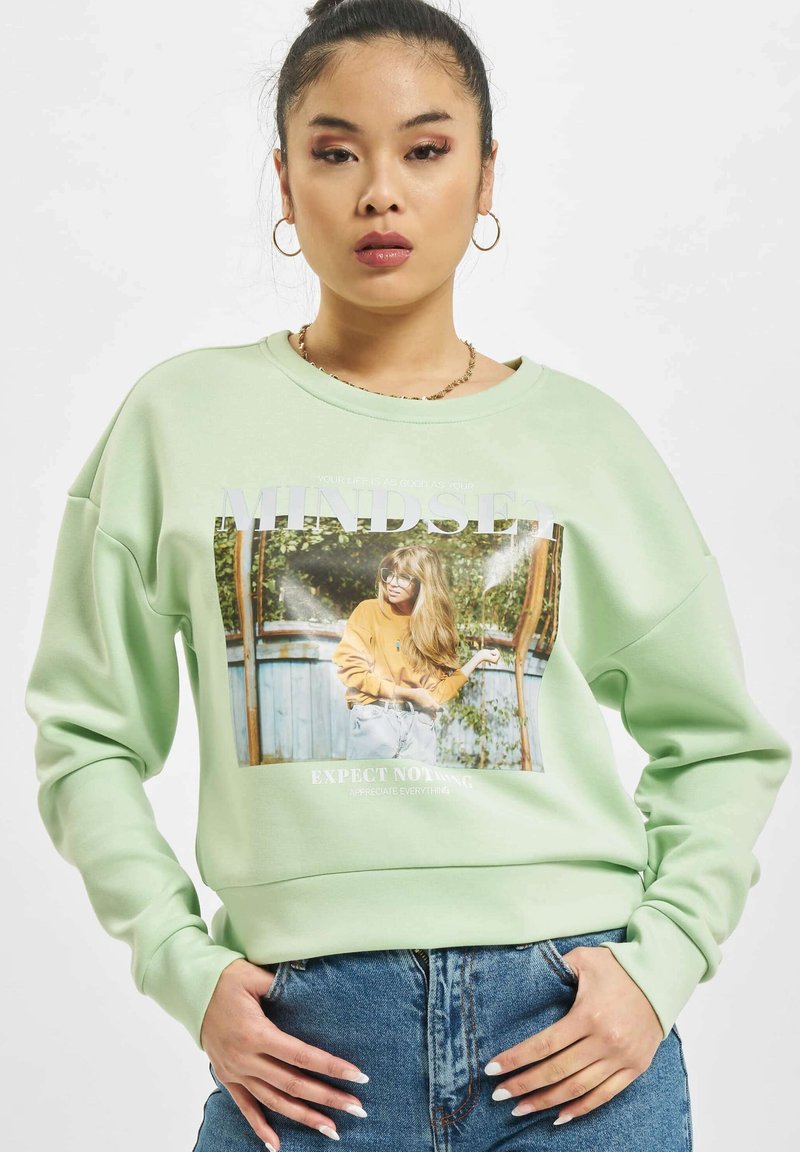 Lys grønn sweatshirt med frontgrafikk, rund hals og avslappet passform. Merkeverdig tekst og bilder komplementerer designet.