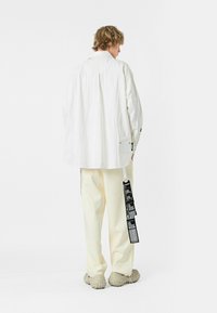 Camisa blanca de gran tamaño con bordado, de corte relajado. Combinada con pantalones color crema, que presentan un acento de etiqueta negra. Calzado texturizado.