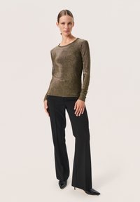 Top a maniche lunghe, aderente, in oro metallico con una texture liscia, abbinato a pantaloni neri a vita alta e tacchi a punta neri.