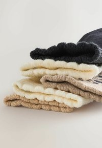 Set of three folded knit socks in black, cream, and tan. Soft, textured fabric with rounded edges and visible stitching details.