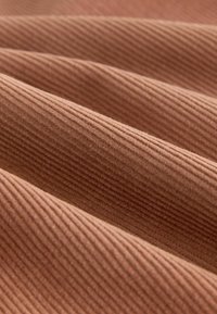 Texturiertes, geripptes Gewebe in einer warmen Terrakottafarbe, das mehrere Falten zeigt, die seine Tiefe und visuelle Anziehungskraft verstärken.