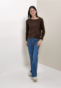 Bruine lange mouwen shirt gecombineerd met blauwe rechte spijkerbroek. De outfit heeft een eenvoudig ontwerp, zacht materiaal en neutraal gekleurde sneakers.