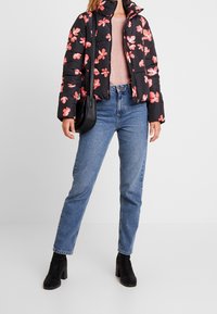 Svart puffjacka med rosa blommönster, dragkedjestängning, hög krage; matchad med ljusblå raka jeans och svarta klackstövlar.