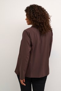 Blazer marron au design ajusté, présentant une texture lisse et des détails de couture subtils. Manches longues et fente arrière visibles.