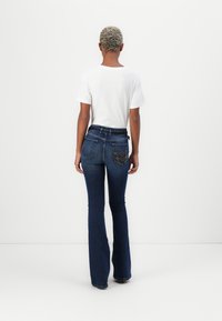 Donkerblauwe wijduitlopende jeans met een kenmerkend geborduurd ontwerp op de achterzak, gecombineerd met een witte t-shirt met korte mouwen.