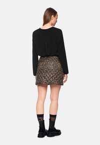 Schwarzes Langarmoberteil, kombiniert mit einem Minirock im Leopardendruck. Das Model trägt schwarze klobige Stiefel mit kontrastierenden Socken. Rückansicht dargestellt.