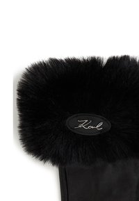 Sorte skinnhansker med en fluffy svart pelsmansjett og en sydd oval etikett med "Karl" i sølvskrift. Myk tekstur og elegant design.