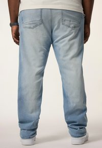 Jeans de denim claros con un corte relajado, que presentan dos bolsillos traseros y un ligero desgastado. Combinados con zapatos blancos y detalles de dobladillo visibles.