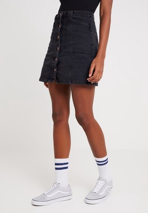 Sort denimnederdel med knapper foran, en lomme med lap, og en let A-formet facon. Brugt med grå sneakers og hvide, stribede sokker.