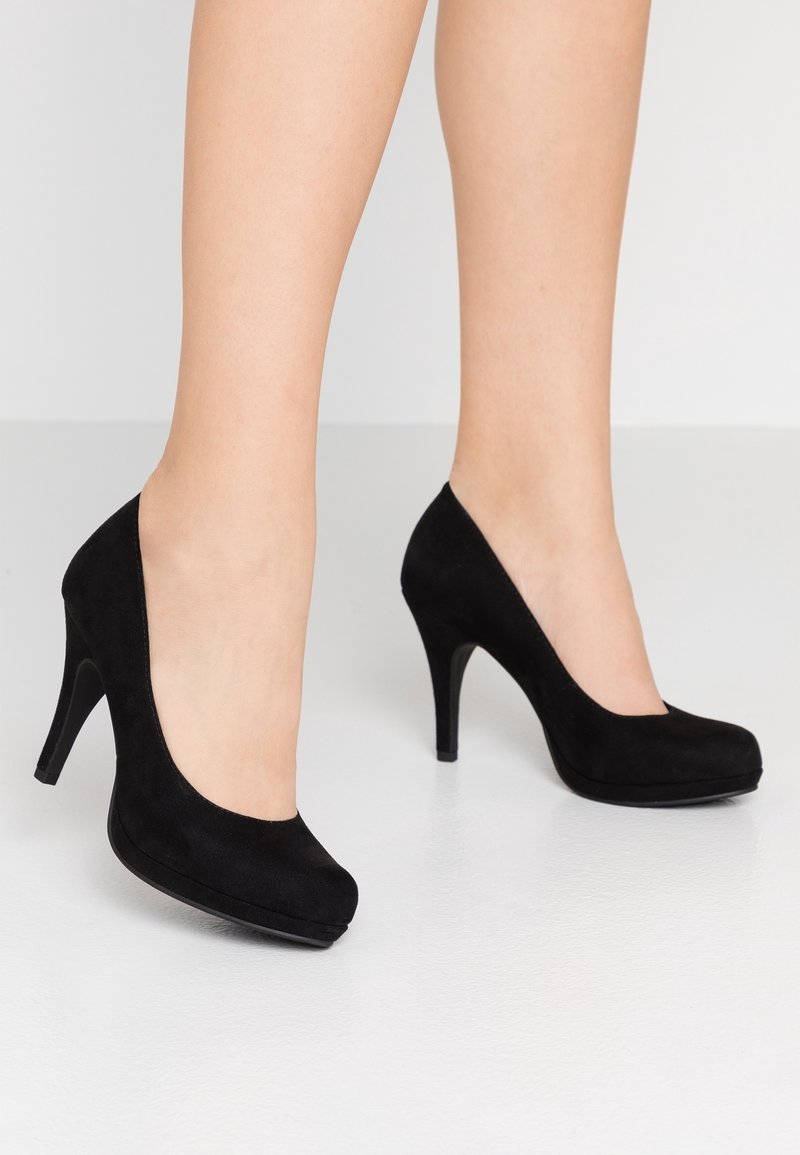 Escarpins en daim noir avec un bout arrondi, un design courbé et un talon aiguille de 10 cm. Texture lisse et accents minimalistes.