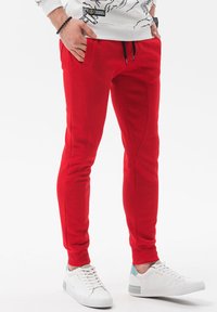 Røde joggerbukser lavet af blødt stof, med en slim fit, to sidelommer og sort snøre. Sammen med hvide sneakers.