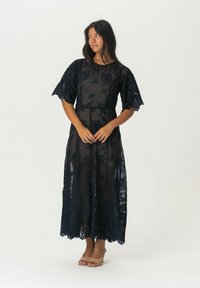 Mustat pitsimekko, jossa on lyhyet röyhelöhiha, hyvin istuva bodice ja valuva hame, jossa on aaltoileva helma. Kevyt, teksturoitu kangas.