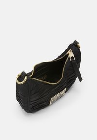 Svart quiltad handväska med guldfärgade detaljer, dragkedjeförslutning och en rektangulär logotypaccent. Slät textur med en strukturerad form.