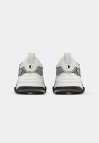 Baskets blanches dotées d'une tige en mesh et d'un col rembourré, avec une semelle noire épaisse et des accents gris sur les côtés.