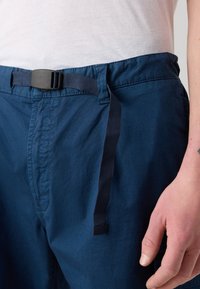 Pantalons décontractés bleu marine en tissu texturé, dotés d'une boucle en plastique noir et d'une ceinture réglable. Comprend un détail de sangle suspendue.