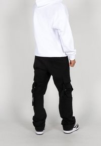 Pantalones cargo negros con múltiples bolsillos y tirantes ajustables, combinados con una sudadera blanca con capucha. Material de mezcla de algodón, corte relajado.