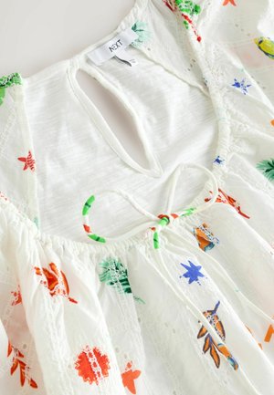 Hvid bomuldsbluse med flerfarvet blomstermotiver. Har en nøglehulåbning, samlet halsudskæring og indviklet blonde detaljer.