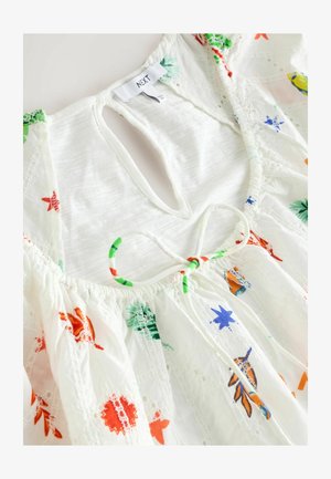 Hvid bomuldsbluse med flerfarvet blomstermotiver. Har en nøglehulåbning, samlet halsudskæring og indviklet blonde detaljer.