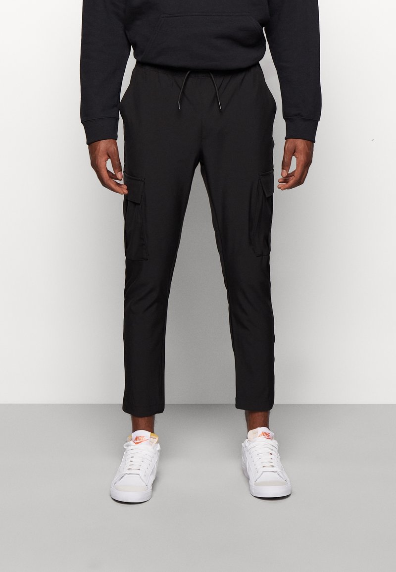 Svarta cargo-byxor med tapered ben, som har två framfickor och elastisk midja. Bärs med vita sneakers. Slät tygkvalitet.