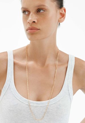 Collar de cadena de clips de papel dorados que se lleva sobre una camiseta sin mangas gris claro, con eslabones alargados y un acabado suave y pulido.