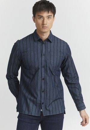 Mørkeblå langermet skjorte med vertikale striper, to brystlommer og knappestolpe foran. Mykt denim stoff med enkle mansjetter.