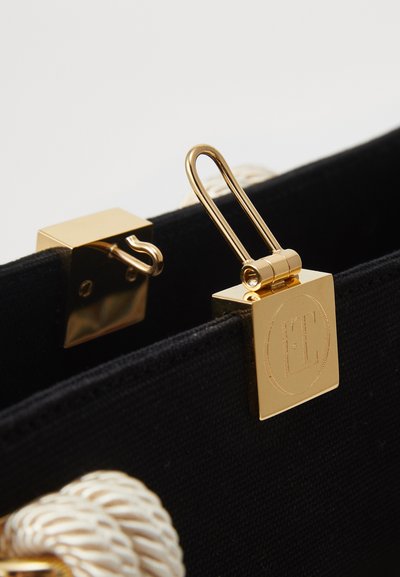 Black fabric handbag with gold hardware, featuring a square metal clasp and textured rope handles. Engraved logo on metal accent.
